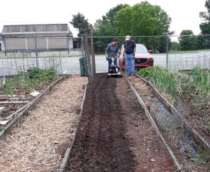 Quina learning to use a new tool in a community garden.