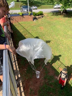 A child dropping a homemade parachute from a second story landing.