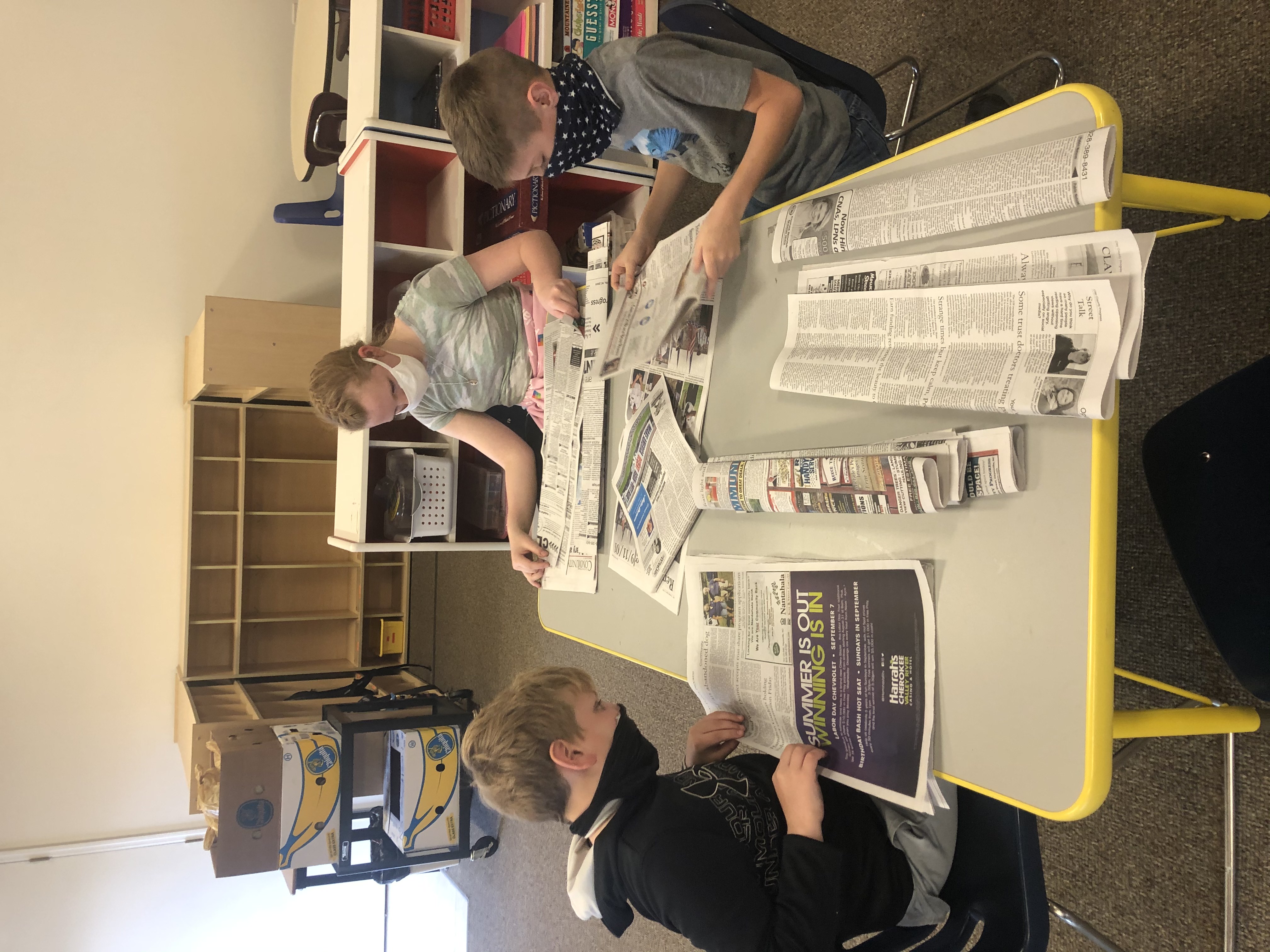 2 boys and a girl folding newspapers.