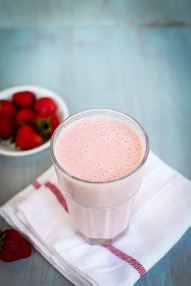 A smoothie in a glass beside a bowl of strawberries.