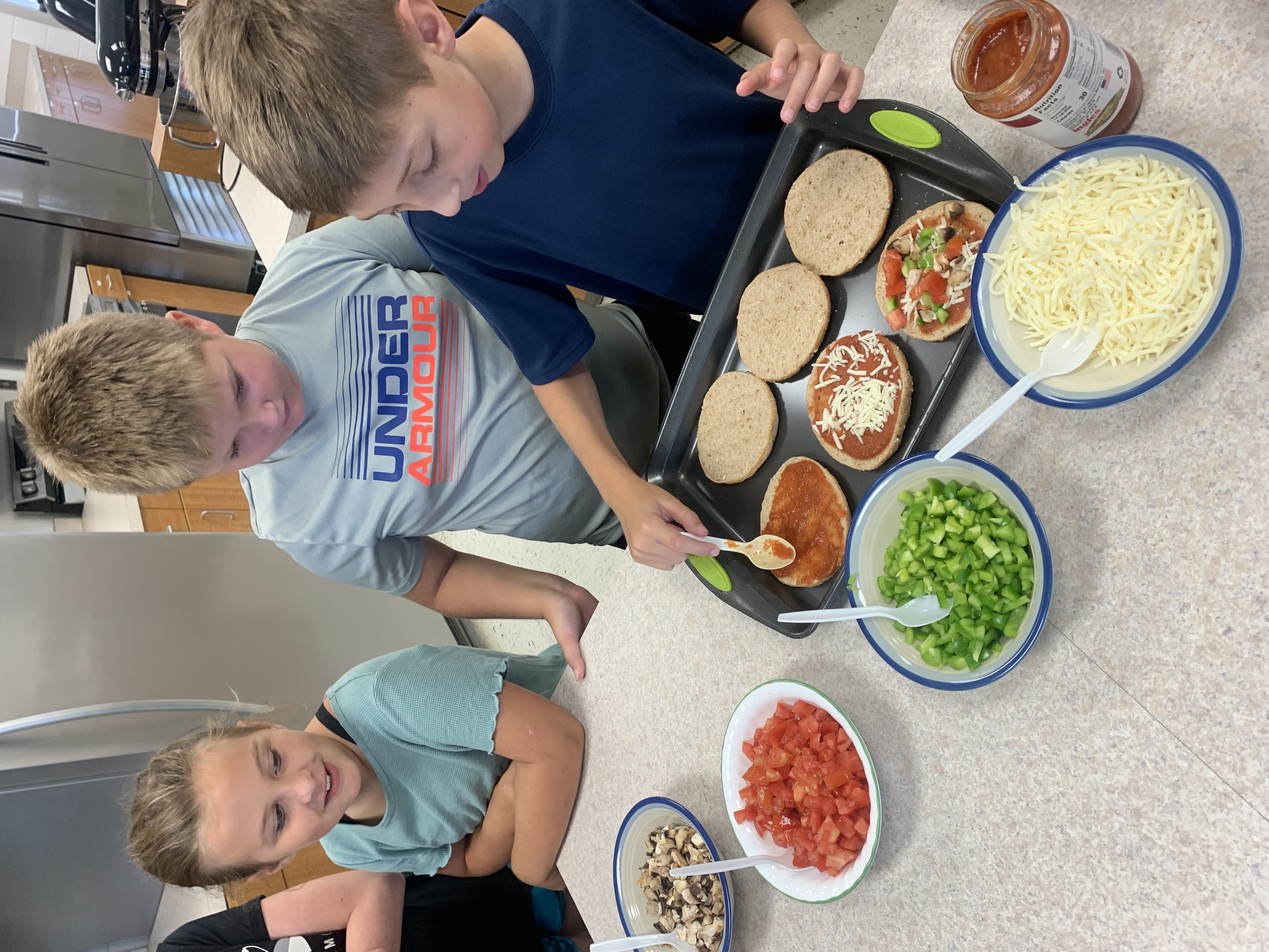 Three children smile over the creation of personal pizzas. 