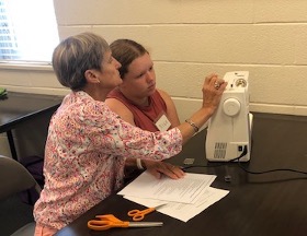 An adult and a teenager inspect a sewing machine on a table.