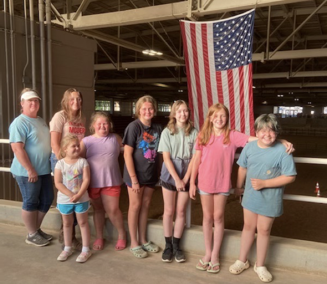 A group of people stand in front of a hanging American flag at a horse clinic.