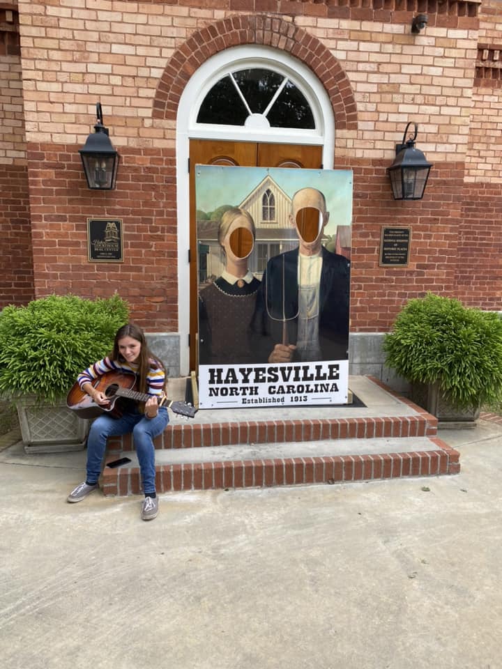young woman on guitar sitting on steps in front of Hayesville NC sign