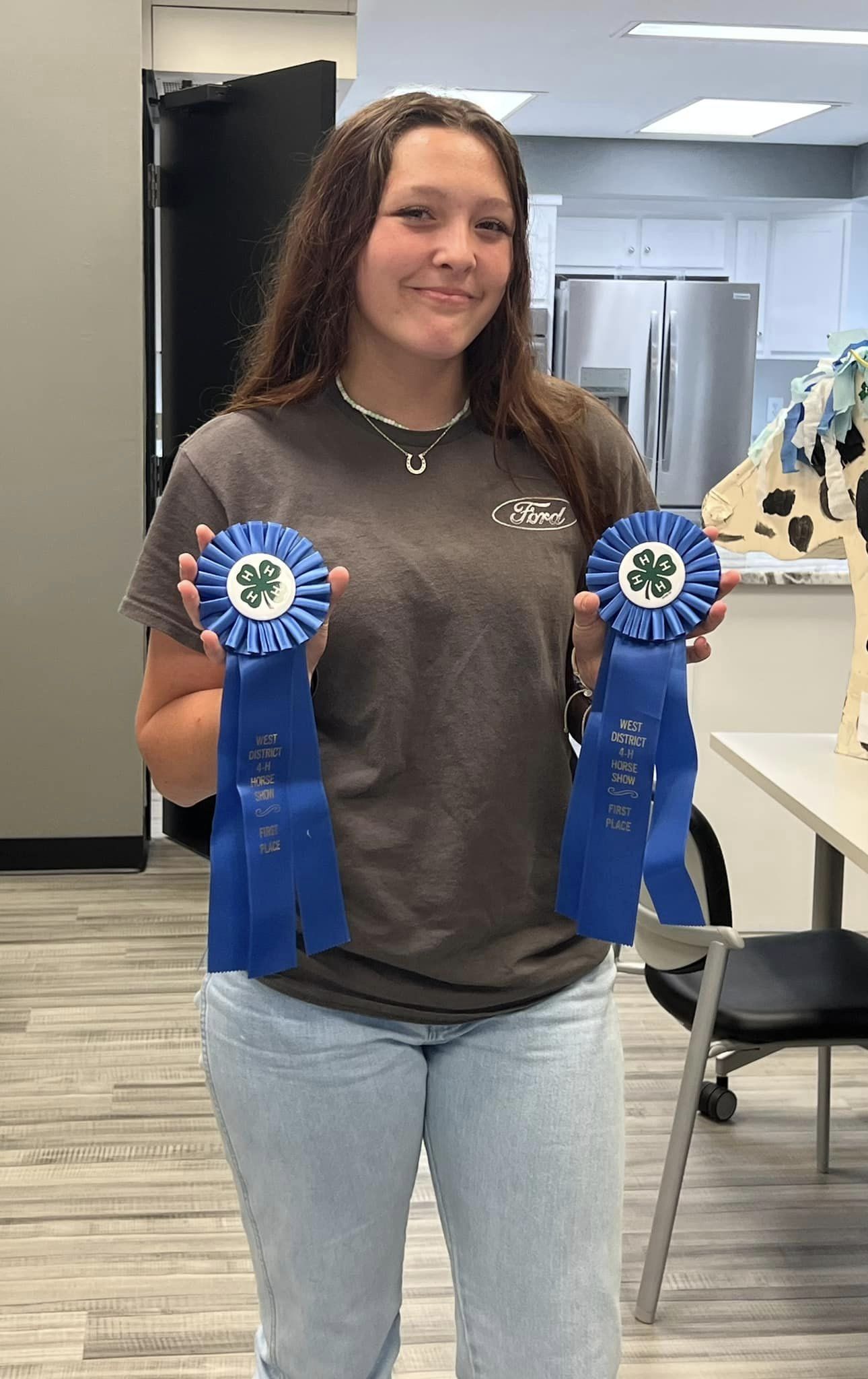 A teenage girl poses with two blue ribbons.