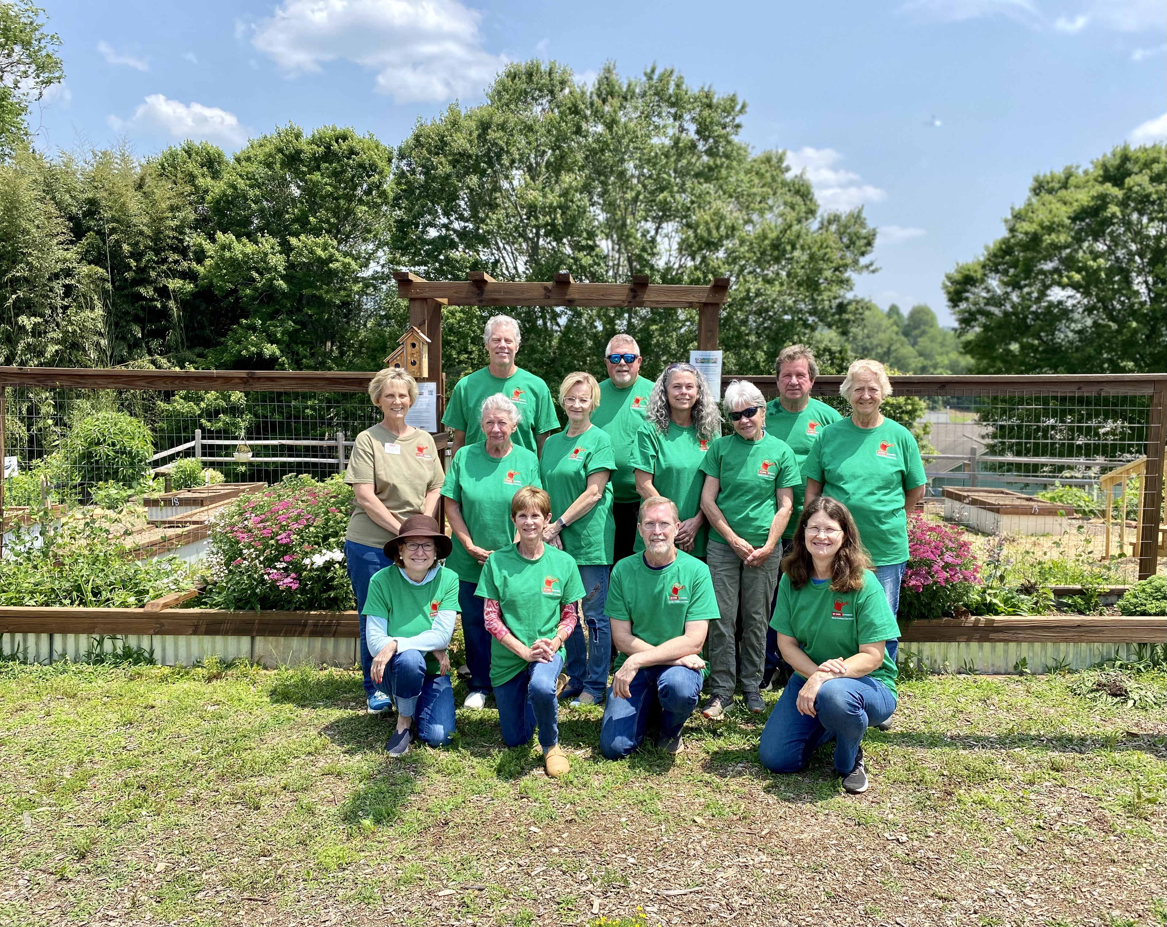 A group of adults in green shirts standing in front of a garden.