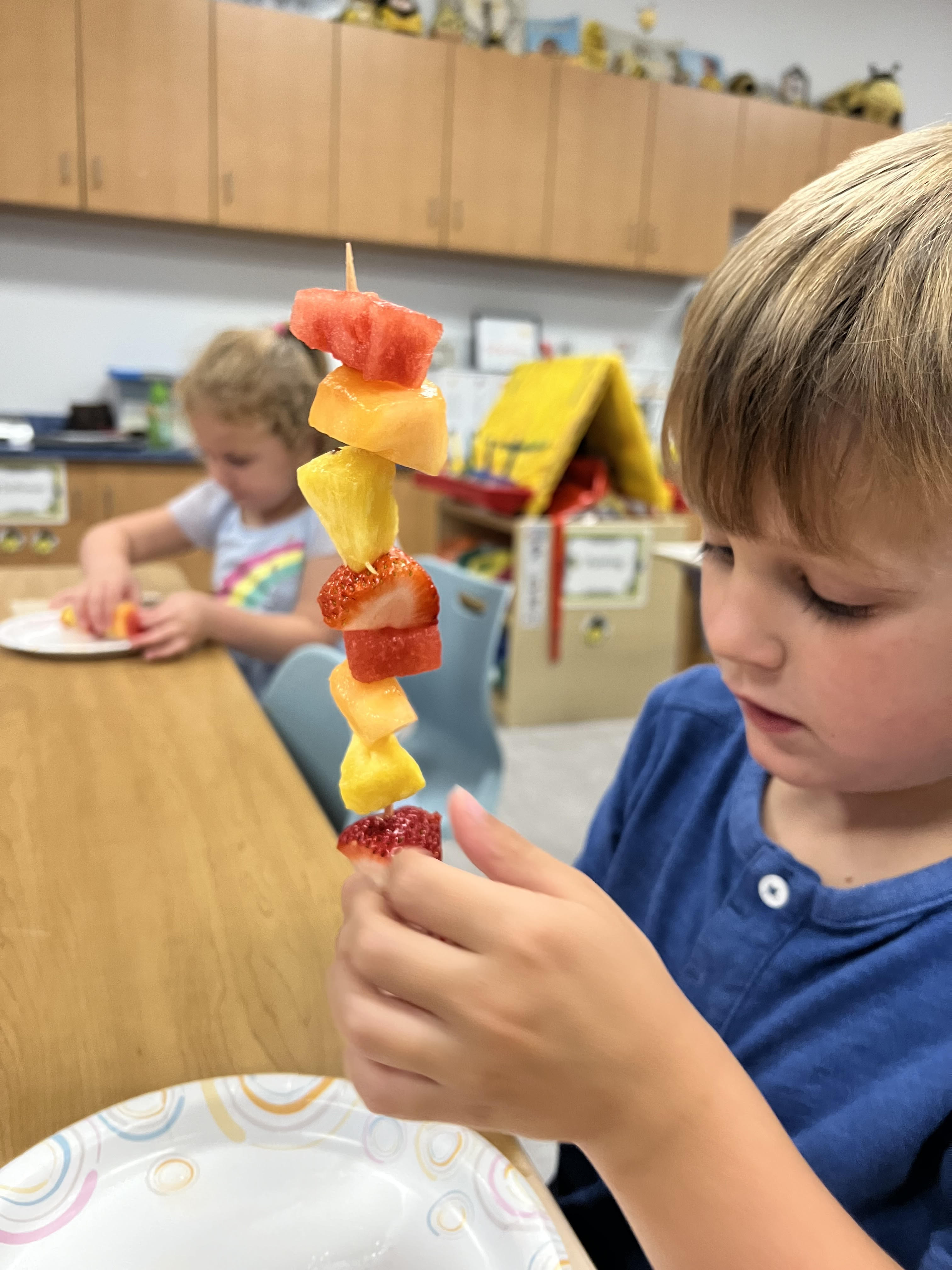 A child adds fruit to a skewer.